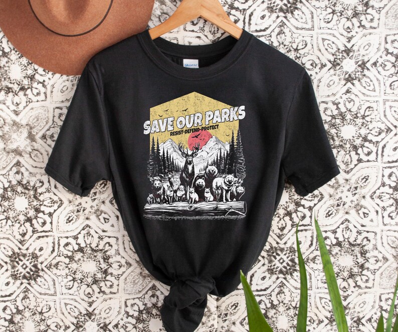 May include: Black t-shirt with a vintage-style graphic that says "Save Our Parks" with a red sun, mountains, and animals. The text below the graphic says "Resist-Defend-Protect".