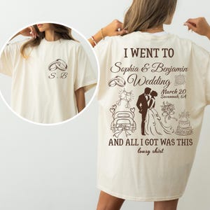 May include: Cream-colored t-shirt with a wedding-themed design. The front features two rings and the initials "S.B." The back displays wedding graphics, including a couple, cake, and text that reads "I WENT TO Sophia & Benjamin Wedding...AND ALL I GOT WAS THIS lousy shirt."