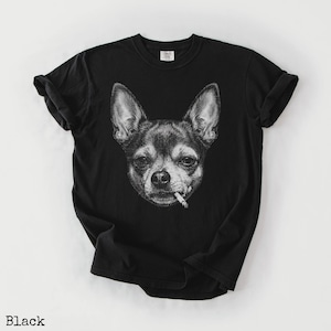 May include: Black t-shirt with a monochrome illustration of a Chihuahua smoking a cigarette. The design is a detailed drawing of the dog's face. The t-shirt has a crew neck and short sleeves. The word "Black" is printed at the bottom.
