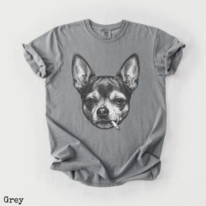 May include: Grey t-shirt with a black and white illustration of a Chihuahua smoking a cigarette. The t-shirt has a crew neck and is made of a soft fabric. The word "Grey" is printed at the bottom of the image.