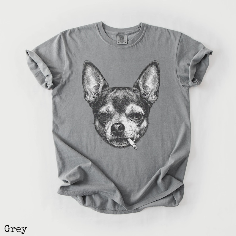 May include: Grey t-shirt with a black and white illustration of a Chihuahua smoking a cigarette. The t-shirt has a crew neck and is made of a soft fabric. The word "Grey" is printed at the bottom of the image.