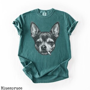 May include: Teal t-shirt with a black and white illustration of a Chihuahua smoking a cigarette. The dog's face is detailed, with visible fur and expression. The shirt has a classic crew neck and short sleeves.