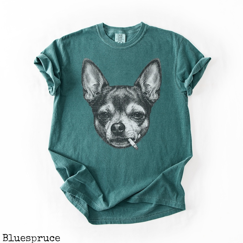 May include: Teal t-shirt with a black and white illustration of a Chihuahua smoking a cigarette. The dog's face is detailed, with visible fur and expression. The shirt has a classic crew neck and short sleeves.