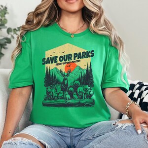 May include: Green t-shirt with a graphic of a forest scene and the text "Save Our Parks Resist-Defend-Protect".