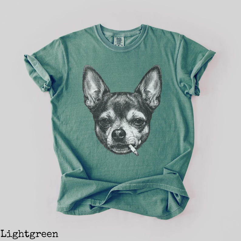 May include: Light green t-shirt with a black and white illustration of a Chihuahua smoking a cigarette. The t-shirt has a crew neck and short sleeves. The text "Lightgreen" is at the bottom of the image.