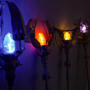 Pode incluir: Quatro cajados de fantasia com cristais brilhantes. O primeiro cajado tem um cristal azul, o segundo um cristal vermelho, o terceiro um cristal amarelo e o quarto um cristal roxo. Cada cajado tem detalhes intrincados e um design único.