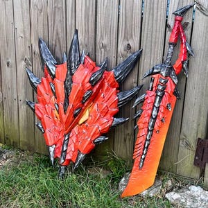 Puede incluir: Un conjunto de escudo y espada con temática de dragón, rojo y negro. El escudo tiene un diseño puntiagudo y en capas con detalles en negro. La espada es larga, con una combinación de colores similar y un borde dentado.