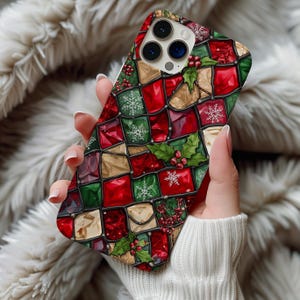 May include: A smartphone case featuring a stained-glass style pattern of red, green, and gold squares. The design includes white snowflake icons, green holly leaves, and clusters of red berries arranged within the grid-like, dark-outlined sections.