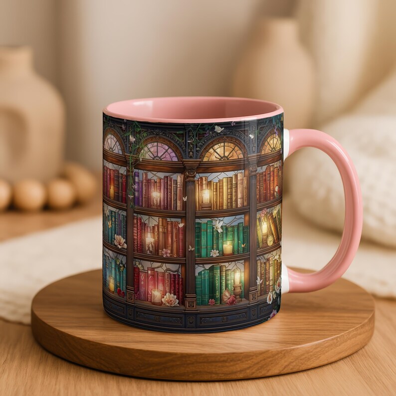 Peut inclure: Un mug en c&eacute;ramique avec un int&eacute;rieur et une anse rose pastel, orn&eacute; d'une illustration enveloppante d'une biblioth&egrave;que en bois &agrave; plusieurs niveaux remplie de livres color&eacute;s, de bougies allum&eacute;es et de petites fleurs blanches.