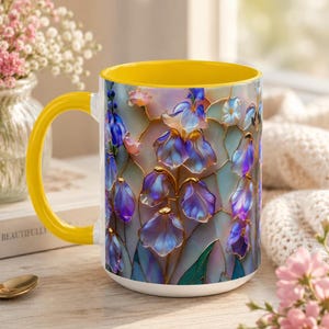May include: A ceramic mug with a bright yellow handle and interior, featuring a colorful stained glass-style pattern of blue and purple bell-shaped flowers on the exterior surface, set against a white base with a smooth, glossy finish.