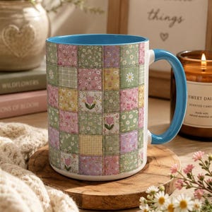 May include: A ceramic mug featuring a patchwork design of various floral and gingham patterns in shades of green, pink, yellow, and white. The mug has a bright blue interior and a matching blue handle, with a repeating motif of small tulips.
