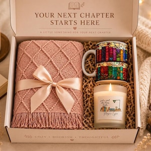 May include: A gift box containing a dusty rose textured throw blanket with a satin ribbon, a ceramic mug with a colorful stained-glass style bookshelf print, and a scented candle with a label reading "just a girl who loves books Megan Lynn".