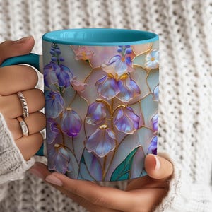 May include: A ceramic mug with a bright turquoise interior and handle, featuring a colorful stained-glass style pattern of purple and blue flowers with gold outlines against a soft, light-colored background of pastel pink and white tones.