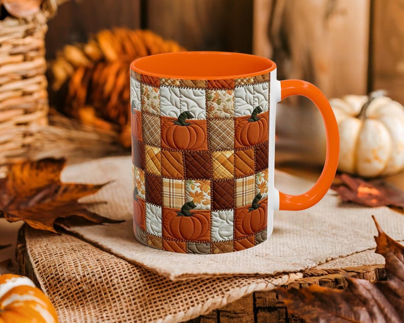 May include: A ceramic mug featuring a patchwork quilt pattern with alternating squares of orange pumpkins, brown plaid, and cream-colored leaves. The mug has a bright orange interior and a matching orange handle, with a quilted texture design.