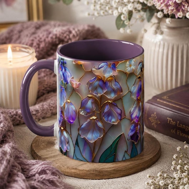 May include: A ceramic mug with a purple interior and handle, featuring a stained-glass style pattern of blue and purple iris flowers with gold outlines. The exterior surface displays a repeating floral motif with translucent petals and green leaves.