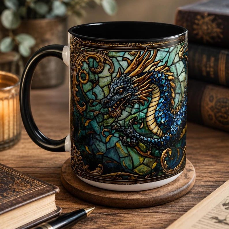 May include: A ceramic mug with a black handle and interior, featuring a vibrant stained glass style illustration of a blue and gold dragon. The exterior surface displays intricate gold filigree patterns surrounding the dragon design.