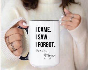 Könnte beinhalten: Weißer Keramikbecher mit schwarzem Innenraum und Henkel. Der Becher zeigt den Text "I CAME. I SAW. I FORGOT." in fetten schwarzen Buchstaben. Darunter steht "See also: Megan" in Schreibschrift.