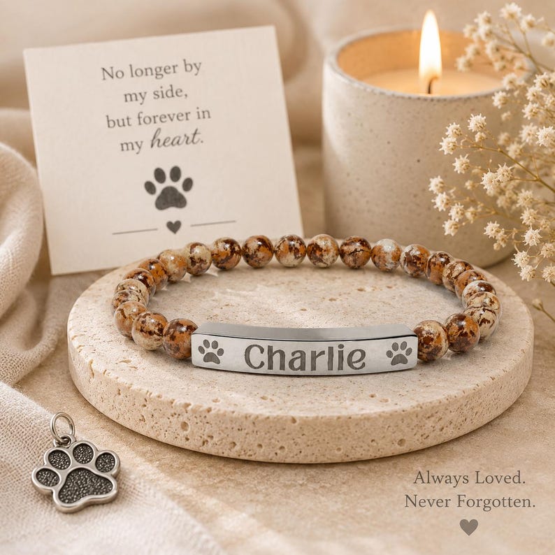 May include: A beaded bracelet with brown and white speckled stones and a silver-toned metal bar engraved with the name Charlie and two paw prints. A separate silver-toned paw print charm is included, alongside a card reading No longer by my side, but forever in my heart.