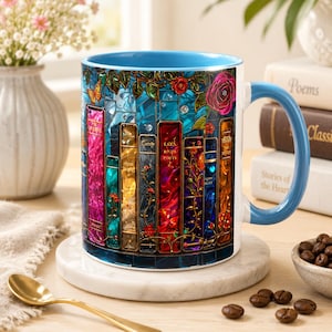May include: A ceramic mug with a light blue interior and handle, featuring a vibrant stained-glass style graphic of colorful book spines, roses, and a butterfly. The design wraps around the exterior, showcasing various hues of red, gold, and blue.