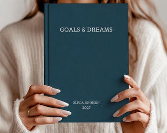 May include: A dark teal hardcover journal with the text GOALS & DREAMS printed in white at the top. The lower portion of the cover features the personalized name OLIVIA JOHNSON and the year 2027 printed in white in a clean, sans-serif font.