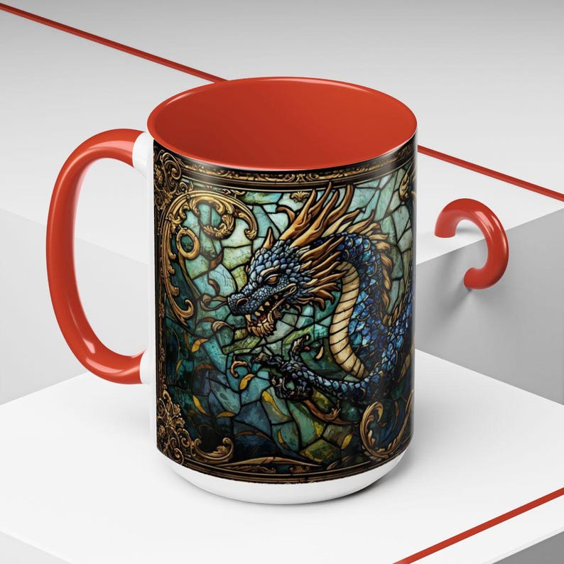May include: A ceramic mug with a bright red handle and interior. The exterior features a detailed graphic of a blue dragon set against a background of teal and green stained glass patterns with ornate gold filigree borders and accents.