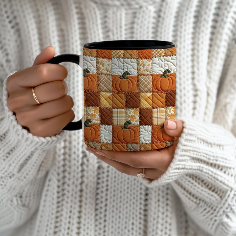 May include: A ceramic mug with a black handle and interior, featuring a repeating patchwork quilt pattern. The design consists of alternating squares in shades of orange, brown, and cream, decorated with pumpkin illustrations and plaid textures.