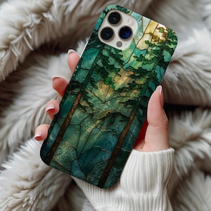 May include: A smartphone case featuring a stained-glass design of a forest scene with tall trees in shades of green, brown, and blue. The case has a glossy finish and a protective design.