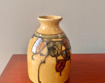 May include: A small, ceramic vase with a rounded body and a narrow neck. The vase is decorated with a floral pattern in shades of brown, green, and orange.