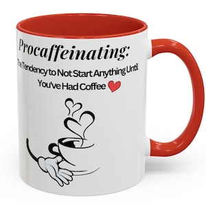 May include: White ceramic coffee mug with a red rim and handle. The mug has a black and white illustration of a coffee cup with steam and the text "Procaffeinating: The tendency to not start anything until you've had coffee".