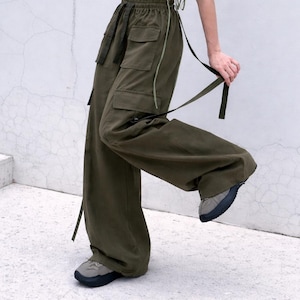 Könnte beinhalten: Olivgrüne Cargohose mit mehreren Taschen und Riemen. Die Hose hat ein weites Bein-Design und wird mit grauen Turnschuhen kombiniert. Ein passendes olivgrünes Crop-Top ist ebenfalls zu sehen.