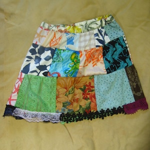May include: A patchwork skirt with a variety of fabric patterns, including floral, nautical, and abstract designs. The skirt features a black lace trim and a white lace accent. The skirt is a mix of colors, including blue, green, orange, and brown.