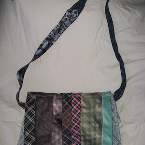 May include: A handmade shoulder bag constructed from various patterned neckties. The bag features a strap with a skull print and a body composed of vertical strips in shades of black, brown, and teal. The bag is a unique accessory.