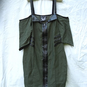 May include: An olive green dress with black leather-like accents and a full-length zipper. The dress features off-the-shoulder sleeves and black straps. A small circular emblem is visible near the neckline. The dress is hanging on a wooden hanger.