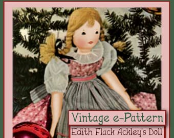 Puede incluir: Patrón vintage para una muñeca, "Para la Navidad de una niña pequeña" 1934, de Edith Flack Ackley. La muñeca lleva un vestido rosa y azul y sostiene un adorno rojo. La muñeca está de pie frente a un árbol de Navidad verde.
