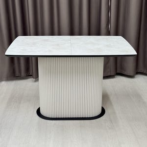 May include: A modern rectangular dining table with a light gray stone-like top and a white, vertically-lined base. The table has a black trim and base. The table is approximately 60 inches long and 36 inches wide.