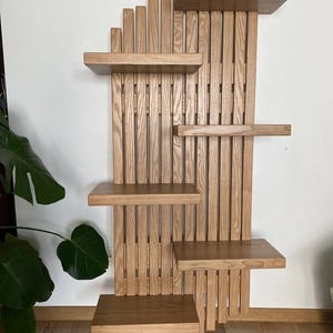 May include: A wooden wall-mounted shelf unit with multiple shelves and vertical slats. The shelves are rectangular and vary in size, offering a display space. The unit is made of light-colored wood, showcasing the natural grain. The design is modern and functional.