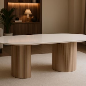 Puede incluir: Mesa de centro ovalada y moderna con tapa color crema y dos patas cilíndricas beige con ranuras verticales. La mesa está sobre una alfombra clara en una habitación luminosa. Dimensiones: aprox. 183 cm de largo y 91 cm de ancho.