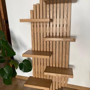 May include: A wooden wall shelf unit with a natural finish. The unit features multiple shelves of varying sizes, arranged in a staggered pattern. The design incorporates vertical wooden slats and horizontal shelves, creating a visually appealing and functional storage solution.