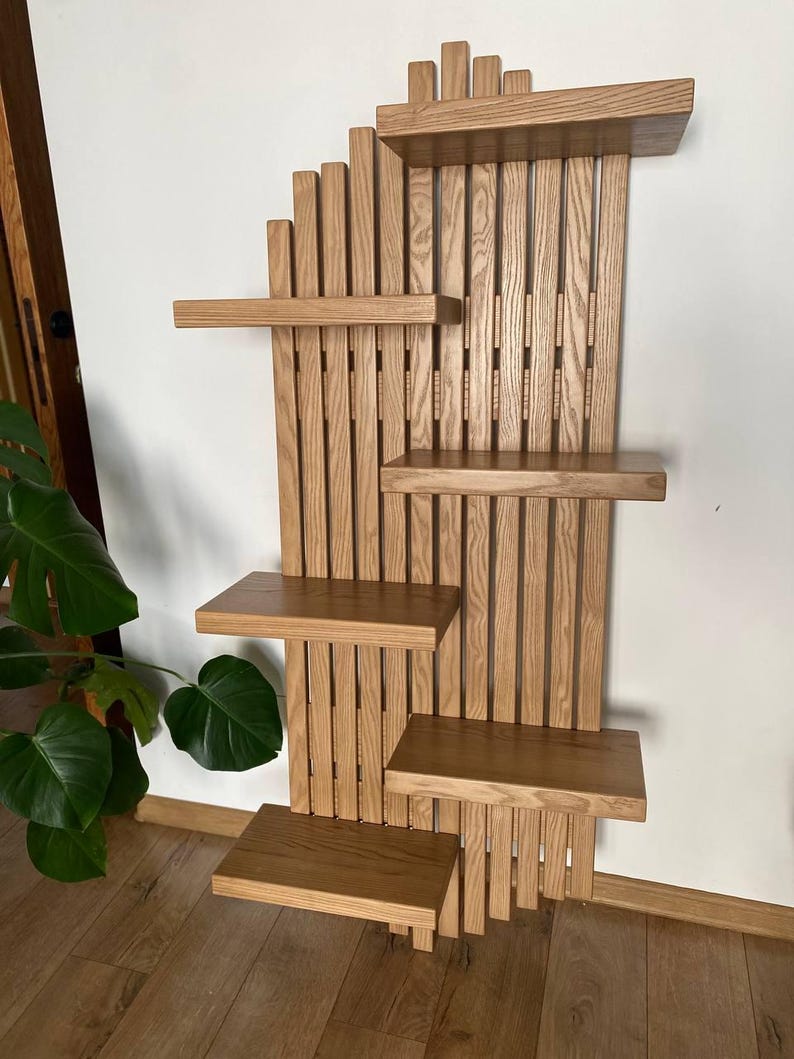 May include: A wooden wall shelf unit with a natural finish. The unit features multiple shelves of varying sizes, arranged in a staggered pattern. The design incorporates vertical wooden slats and horizontal shelves, creating a visually appealing and functional storage solution.