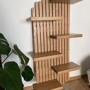 May include: A wooden wall-mounted cat shelf with multiple platforms. The shelves are rectangular and arranged in a staggered pattern. The wood has a natural, light brown finish, and the design incorporates vertical slats for a modern look. The shelf is designed for cats to climb and rest.