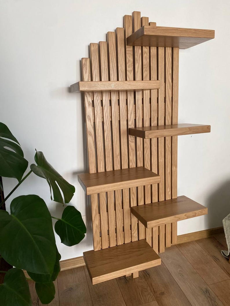 May include: A wooden wall-mounted cat shelf with multiple platforms. The shelves are rectangular and arranged in a staggered pattern. The wood has a natural, light brown finish, and the design incorporates vertical slats for a modern look. The shelf is designed for cats to climb and rest.