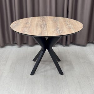 May include: A round wooden table with a black X-shaped base. The table top has a light wood grain pattern.
