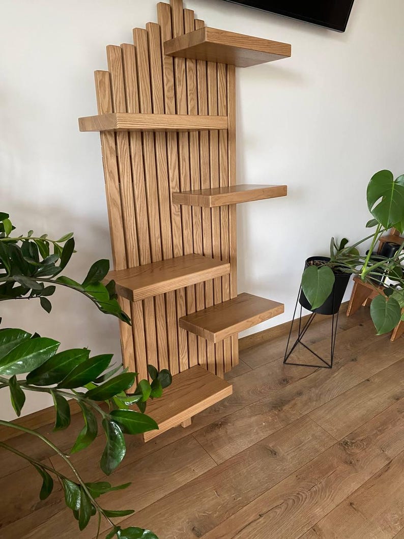 May include: A wooden wall-mounted shelf unit with multiple shelves of varying sizes. The unit is made of light-colored wood and features a vertical slatted design. The shelves are arranged in an asymmetrical pattern, suitable for displaying plants or decor.
