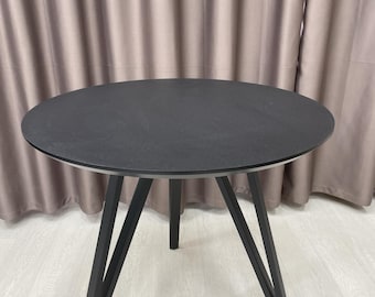 May include: A round, black table with a textured surface. The table has three angled legs. The table is approximately 30 inches in diameter.