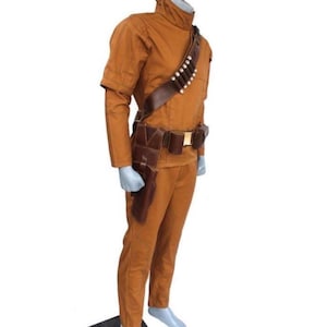 Może przedstawiać: Brązowy kostium z wysokim kołnierzem, długimi rękawami i pasującymi spodniami. Kostium zawiera brązowy sk&oacute;rzany pasek z sakiewkami i kaburą oraz bandolier z białymi kulami. Str&oacute;j jest prezentowany na manekinie.