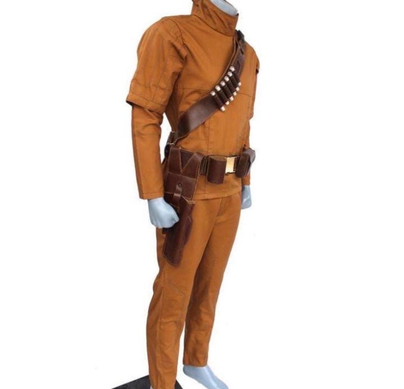 Może przedstawiać: Brązowy kostium z wysokim kołnierzem, długimi rękawami i pasującymi spodniami. Kostium zawiera brązowy sk&oacute;rzany pasek z sakiewkami i kaburą oraz bandolier z białymi kulami. Str&oacute;j jest prezentowany na manekinie.