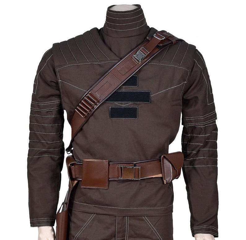 May include: Brown costume with a high collar, shoulder strap, and belt. The costume has white stitching details and black patches on the chest. A brown leather holster and pouch are attached to the belt.