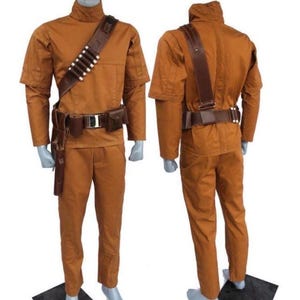 Może przedstawiać: Dwuczęściowy kostium w ciepłym brązowym kolorze, składający się z koszuli z długim rękawem z wysokim kołnierzem i pasujących spodni. Kostium zawiera brązowy sk&oacute;rzany pasek, pasek na ramię z białymi akcentami i kaburę. Wyświetlany na manekinie.