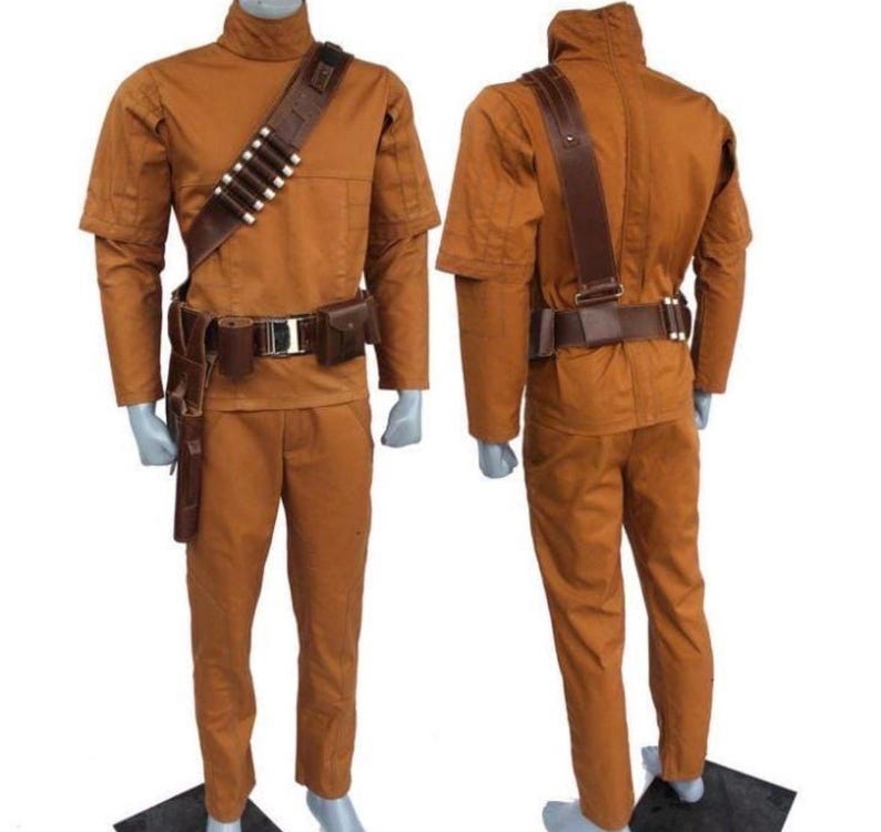 Może przedstawiać: Dwuczęściowy kostium w ciepłym brązowym kolorze, składający się z koszuli z długim rękawem z wysokim kołnierzem i pasujących spodni. Kostium zawiera brązowy sk&oacute;rzany pasek, pasek na ramię z białymi akcentami i kaburę. Wyświetlany na manekinie.