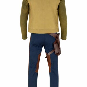 K&ouml;nnte beinhalten: Ein Kost&uuml;mset mit einer beigefarbenen Jacke mit olivgr&uuml;nen &Auml;rmeln, einer marineblauen Hose mit braunen Akzenten und einem braunen Holster. Die Jacke hat einen Stehkragen. Die Hose hat braune Eins&auml;tze an den Seiten.